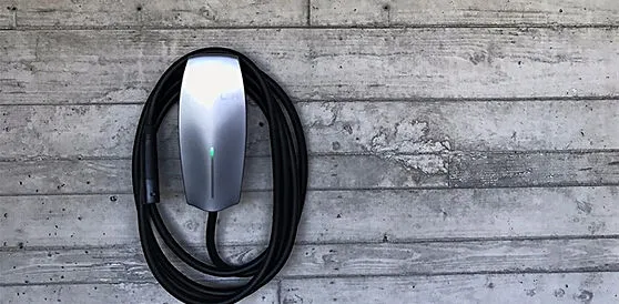 Coiled electric vehicle connector mounted on a wood wall.